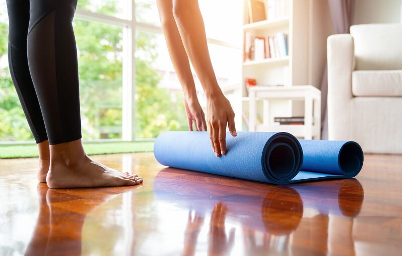 woman rolling up a blue foam yoga mat in her living room